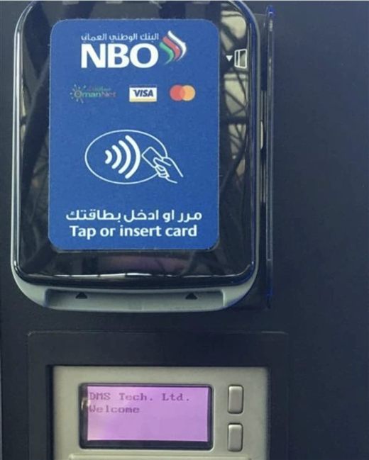 Muscat: the bank's own reader — Tap or insert card, in Arabic and English, over the national payment network — and on the display beneath it, "DMS Tech. Ltd. Welcome"